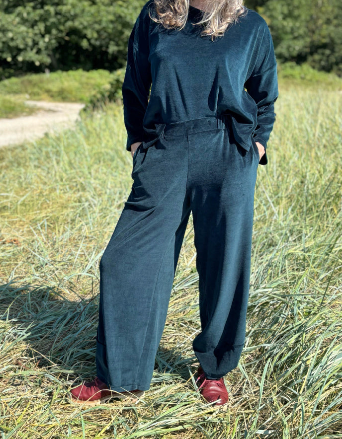 Person wearing teal velvet pants and red shoes standing in a grassy field.