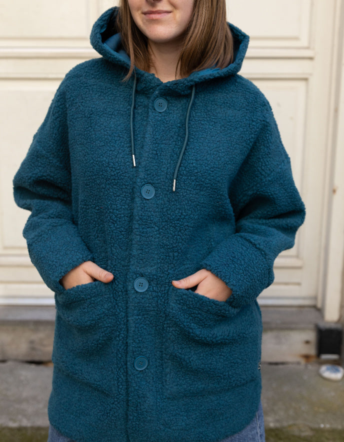 Person wearing a blue hooded coat standing against a neutral background