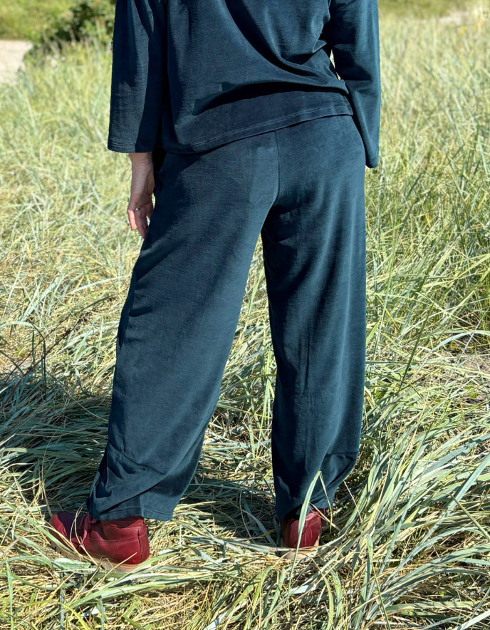 Person wearing teal velvet pants and red shoes standing in a grassy field.