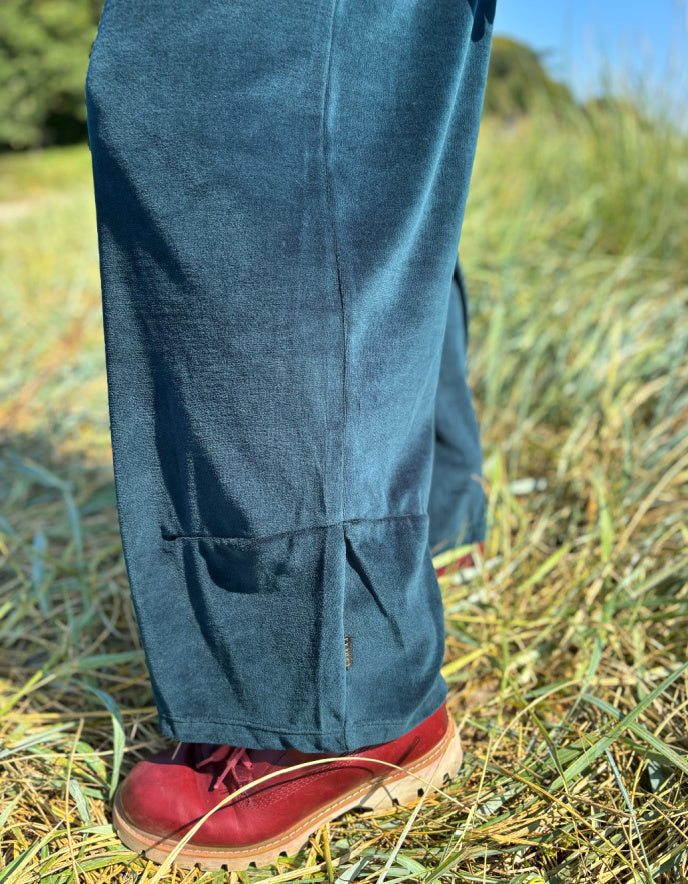 Person wearing teal velvet pants and red shoes standing in a grassy field.