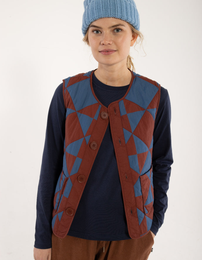 Person wearing a blue and red patterned vest over a dark shirt with a white background