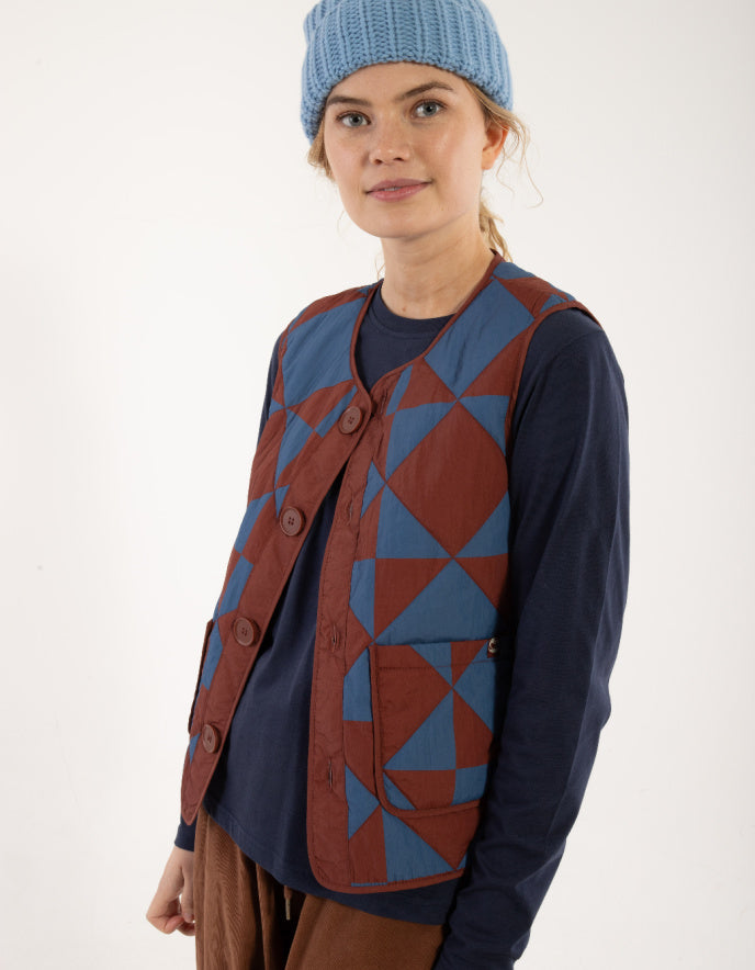 Person wearing a patterned vest and blue beanie on a white background