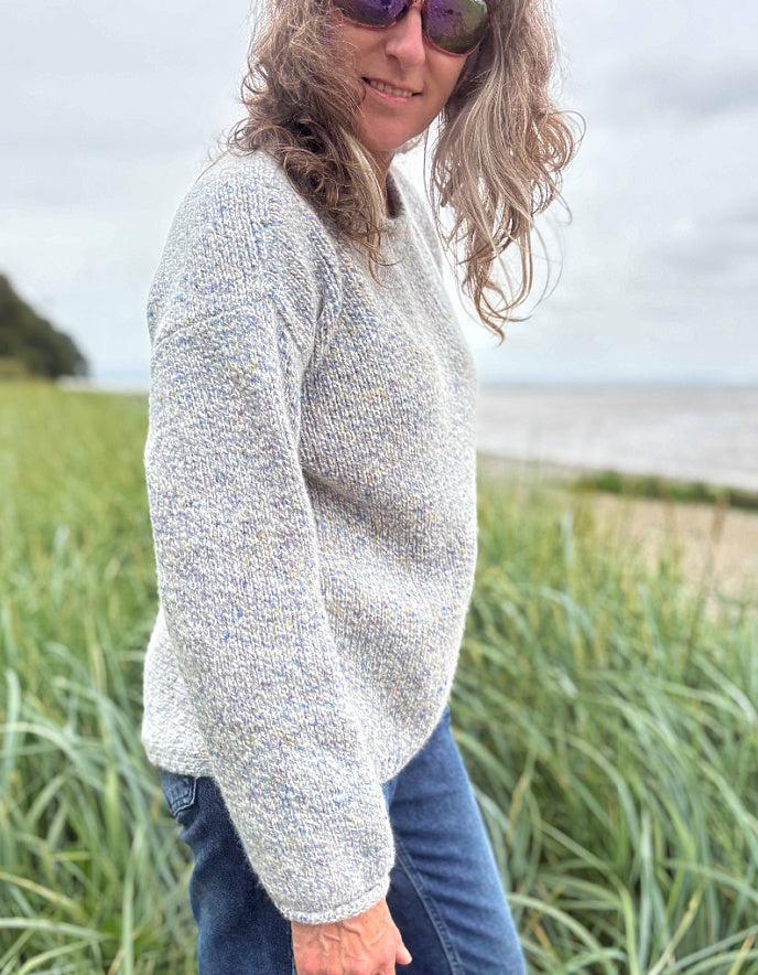 Person wearing a silver grey donegal tweed sweater and sunglasses standing in a grassy field with a cloudy sky.