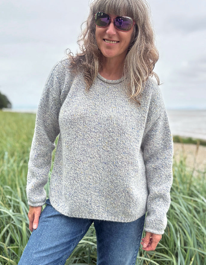 Person wearing a silver grey donegal tweed sweater and sunglasses standing in a grassy field with a cloudy sky.
