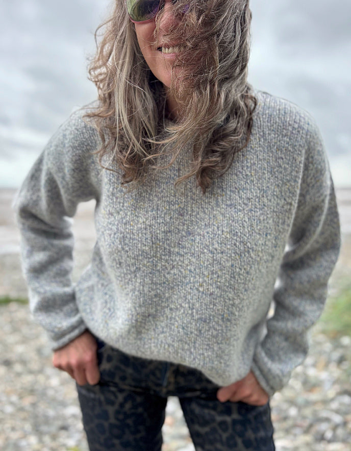 Person wearing a silver grey donegal tweed sweater and sunglasses standing in a grassy field with a cloudy sky.