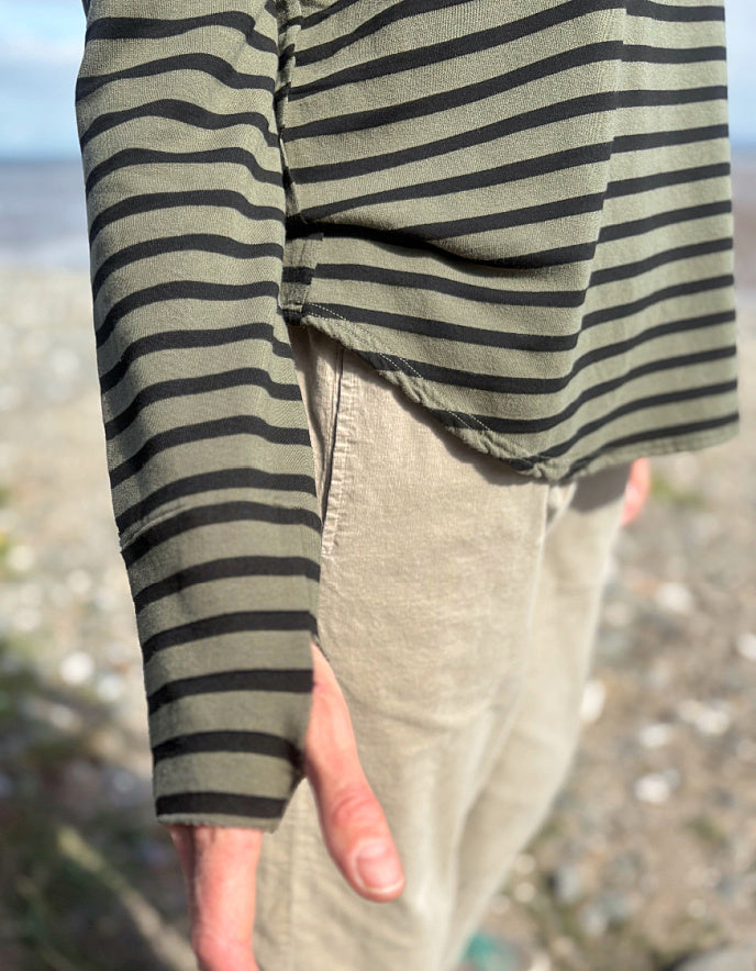 Person wearing a striped shirt and beige pants with a blurred natural background