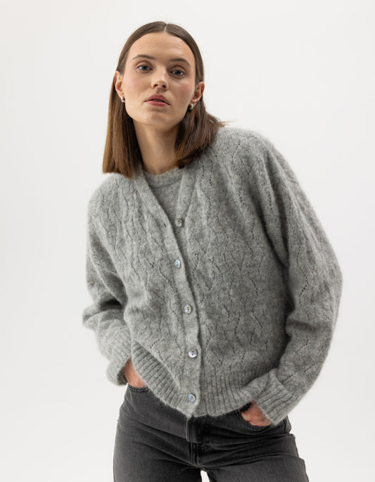 Woman wearing a gray cable knit cardigan on a white background