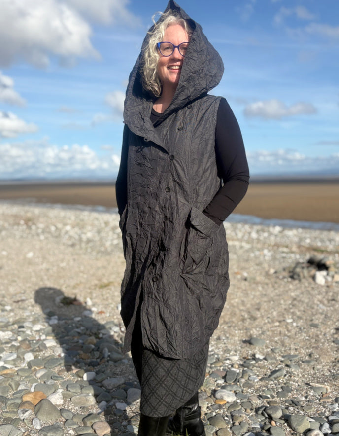 Person wearing a long dark coat on a beach with a blue sky and clouds in the background
