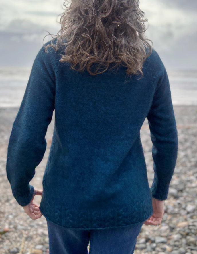 Person wearing a blue textured sweater on a pebbly beach