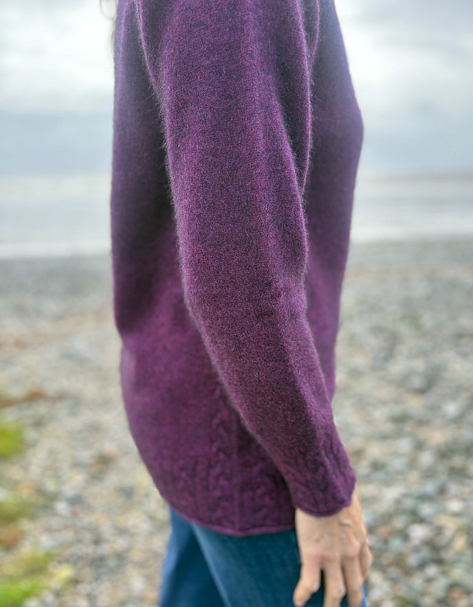 Person wearing a purple sweater with a blurred background of a beach.