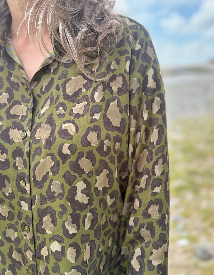 Person wearing a green leopard print shirt with a blurred natural background