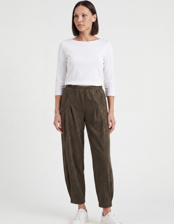 A woman modeling a white long-sleeve top and dark olive green wide-leg trousers against a plain white studio background.