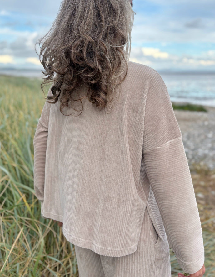 Person wearing a winter white jumbo cord jacket and sunglasses on a beach with grass and water in the background
