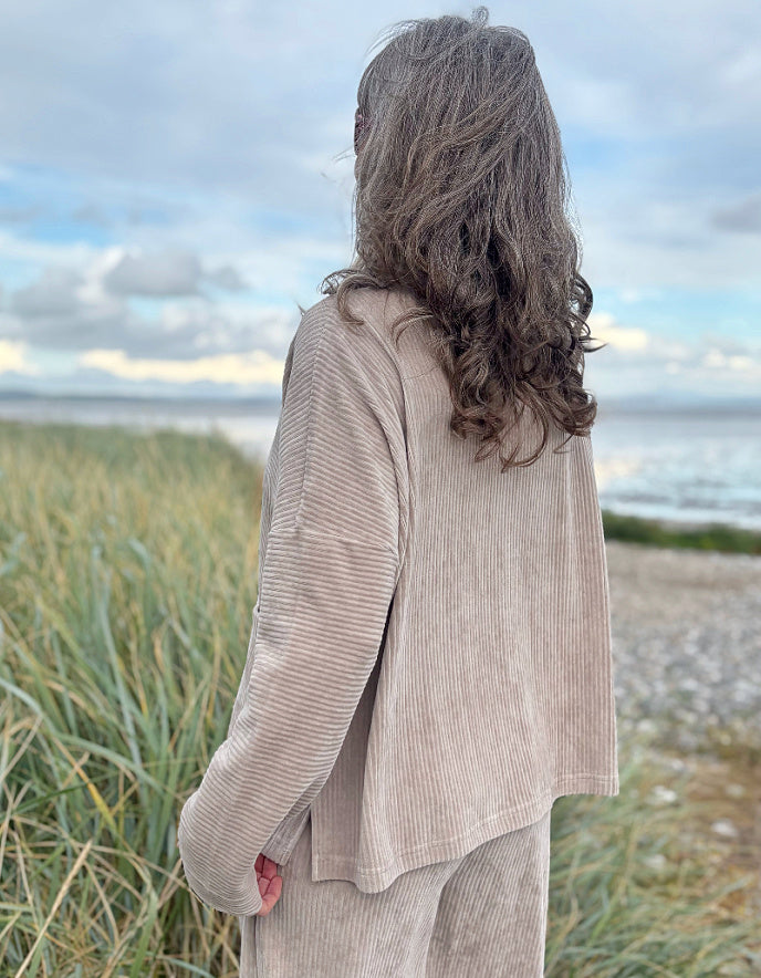 Person wearing a winter white jumbo cord jacket and sunglasses on a beach with grass and water in the background