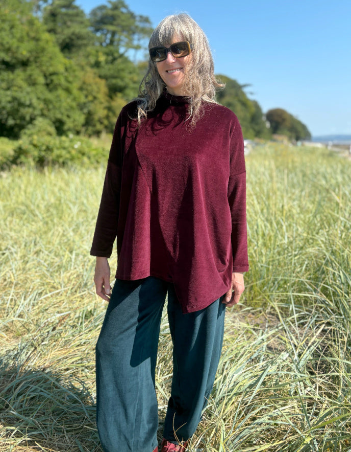 Woman in a burgundy velvet co-ord trouser and top outfit standing in a field with trees in the background