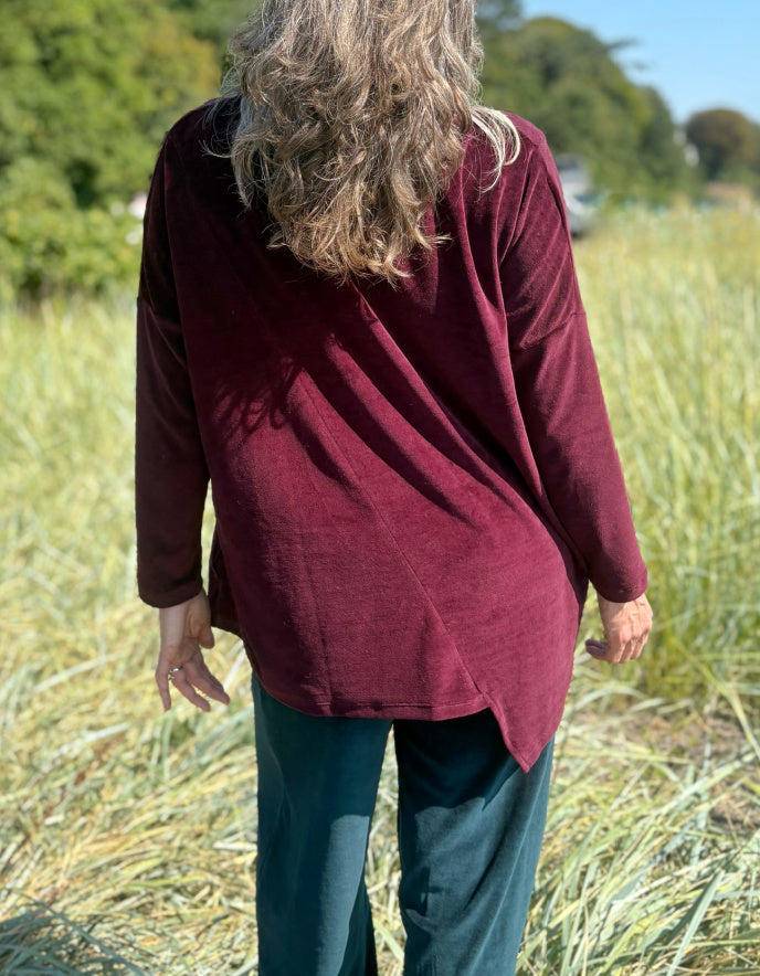 Woman in a burgundy velvet co-ord trouser and top outfit standing in a field with trees in the background