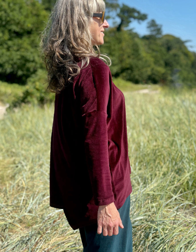 Woman in a burgundy velvet co-ord trouser and top outfit standing in a field with trees in the background