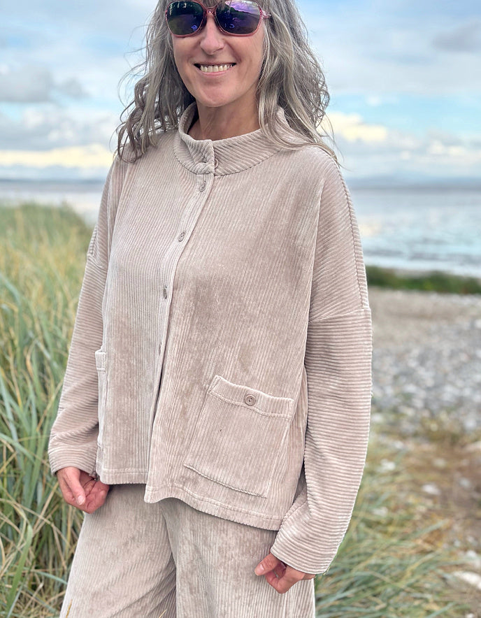 Person wearing a winter white jumbo cord jacket and sunglasses on a beach with grass and water in the background