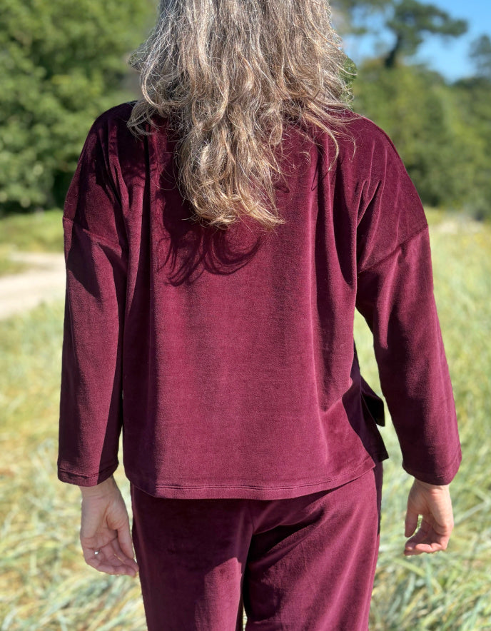 Person wearing a burgundy velvet co-ord outfit standing in a field with trees in the background