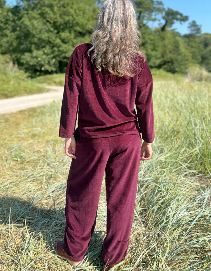Person wearing a burgundy velvet coord outfit standing in a grassy field with trees in the background