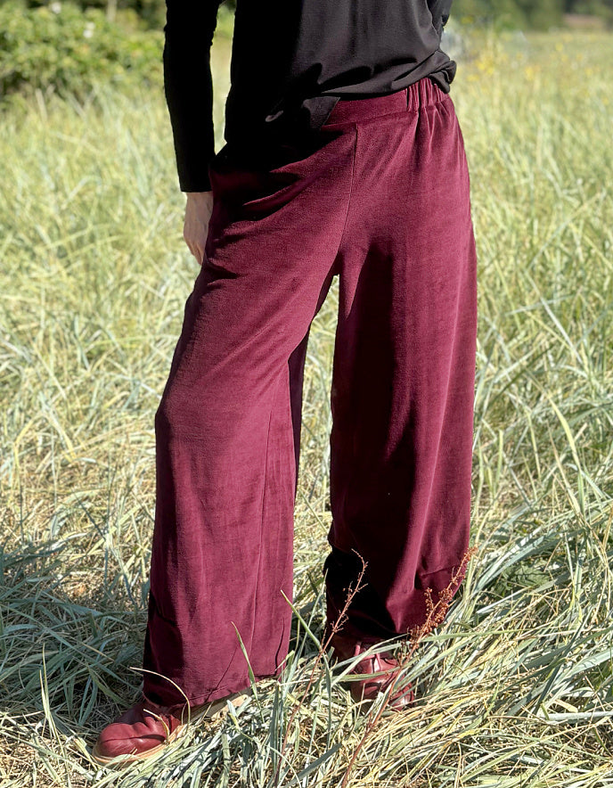 Woman wearing a black top and burgundy velvet pants standing in a grassy field.