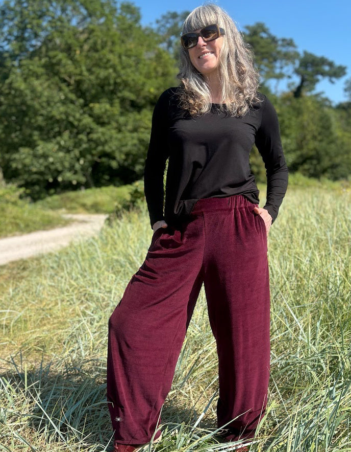 Woman wearing a black top and burgundy velvet pants standing in a grassy field.