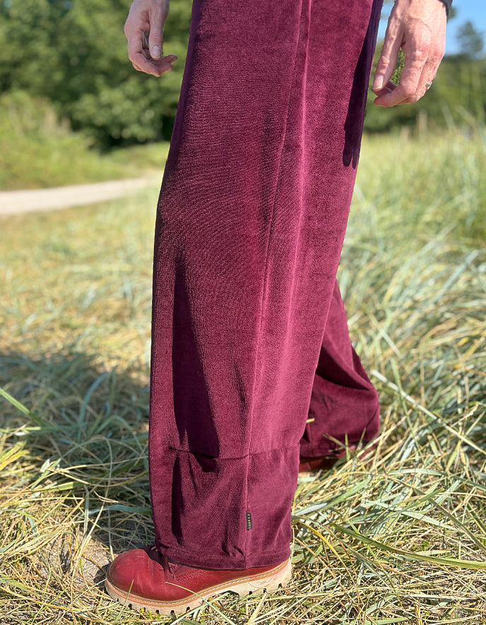Woman wearing a black top and burgundy velvet pants standing in a grassy field.