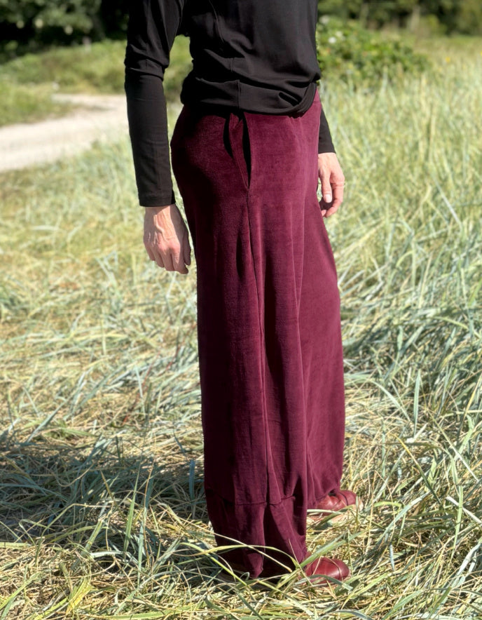 Woman wearing a black top and burgundy velvet pants standing in a grassy field.