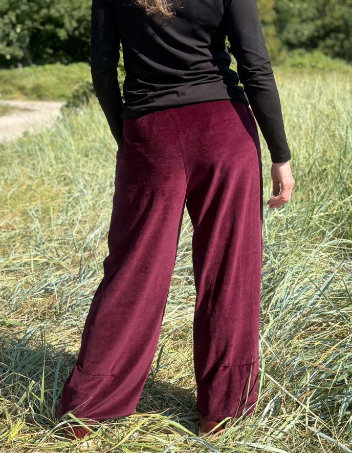 Woman wearing a black top and burgundy velvet pants standing in a grassy field.