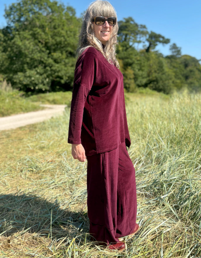 Woman in a burgundy velvet co-ord trouser and top outfit standing in a field with trees in the background