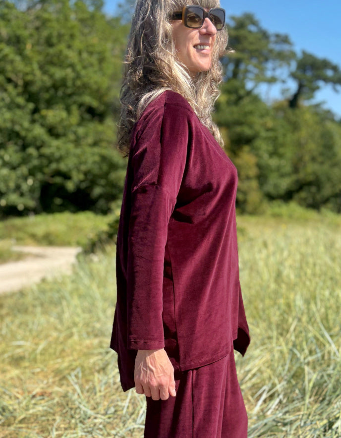 Woman in a burgundy velvet co-ord trouser and top outfit standing in a field with trees in the background