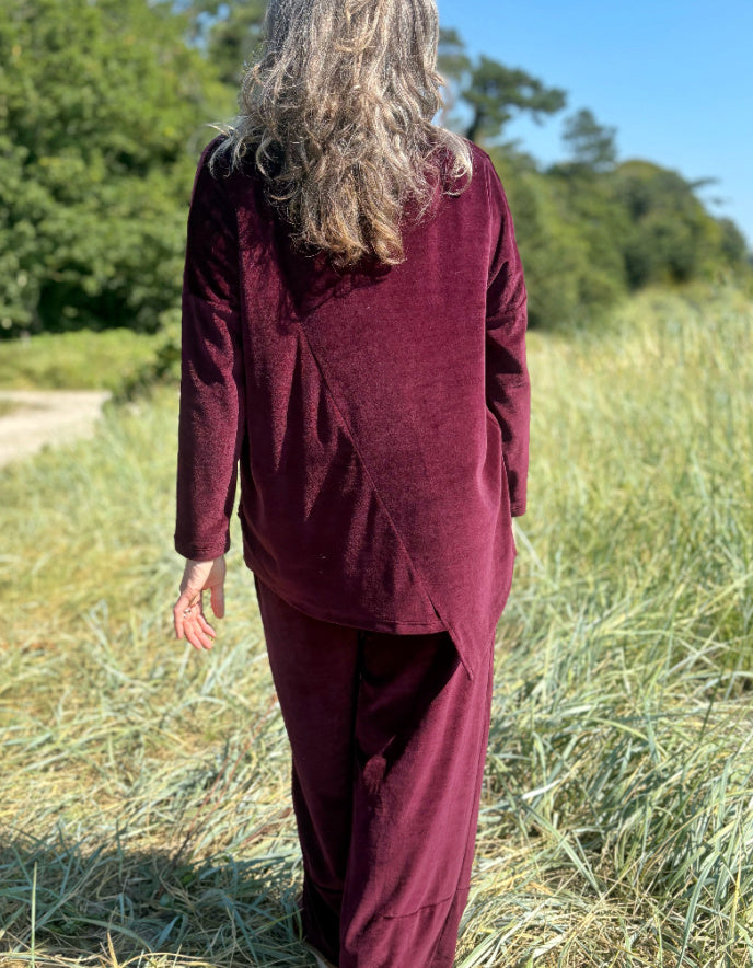 Woman in a burgundy velvet co-ord trouser and top outfit standing in a field with trees in the background