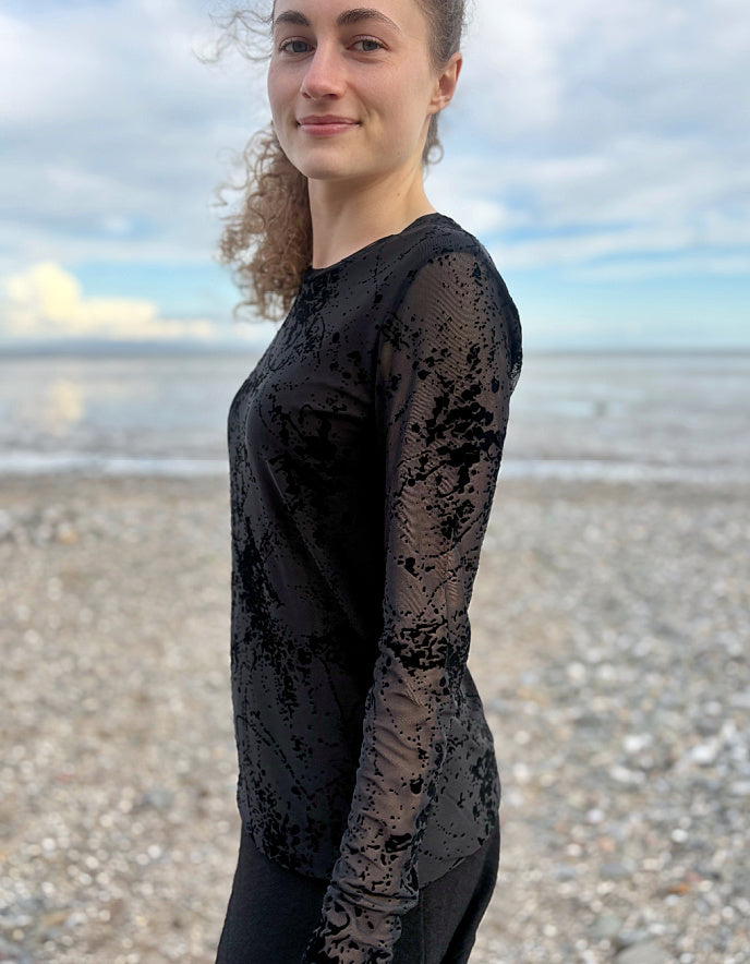 Person wearing a black long-sleeve top with sheer overlay on a beach.