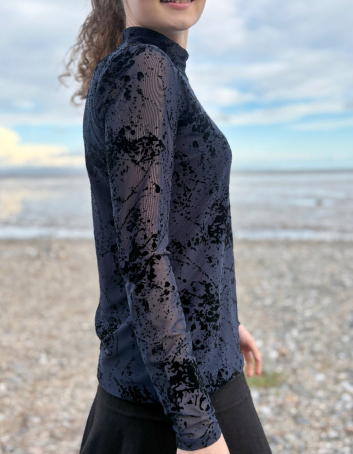 lady wearing tight fit navy mesh top with velvet splatter overlay print with a black skirt on a beach