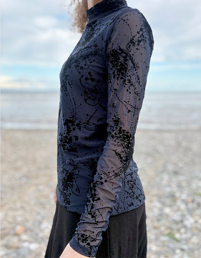 lady wearing tight fit navy mesh top with velvet splatter overlay print with a black skirt on a beach