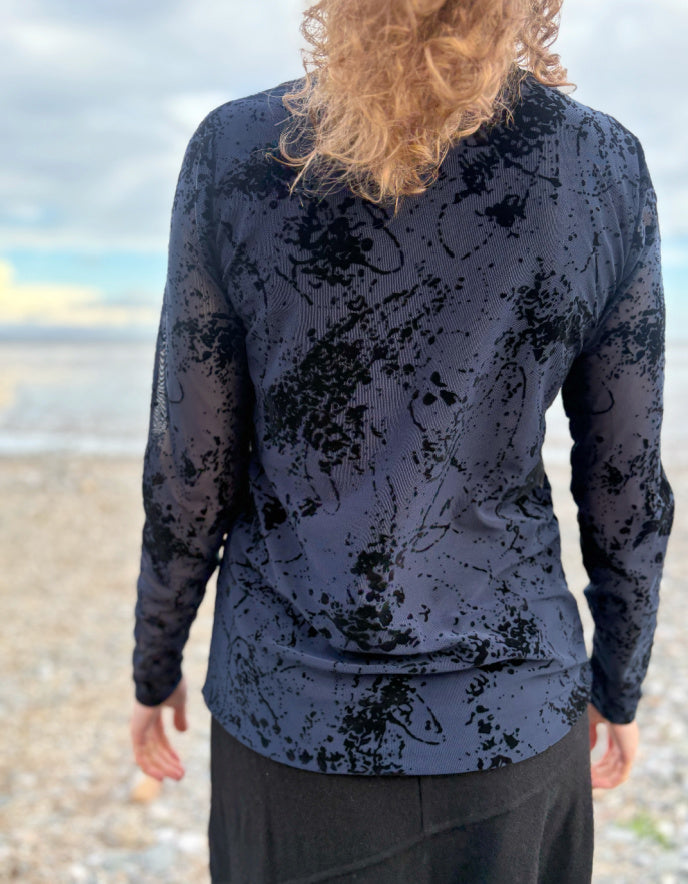 lady wearing tight fit navy mesh top with velvet splatter overlay print with a black skirt on a beach