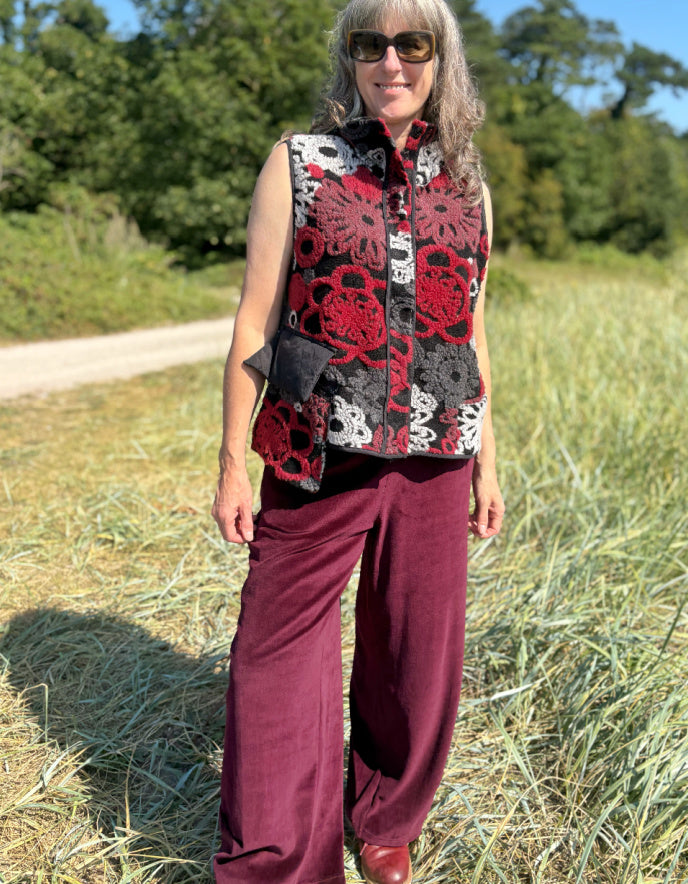 Woman wearing a floral patterned vest and burgundy pants standing in a field.