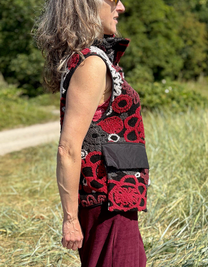 Woman wearing a floral patterned vest and burgundy pants standing in a field.
