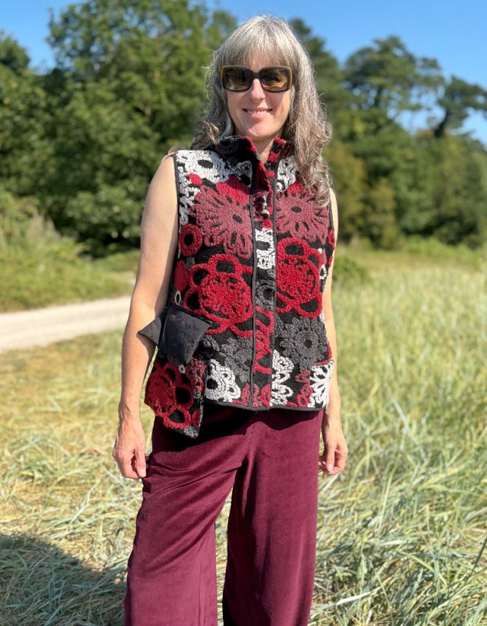 Woman wearing a floral patterned vest and burgundy pants standing in a field.