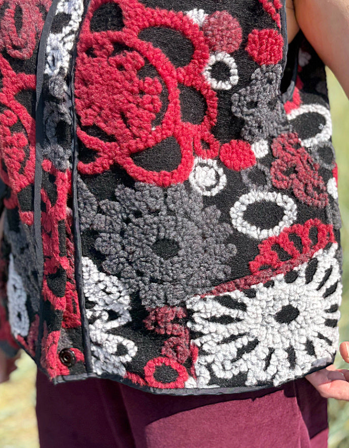 Woman wearing a floral patterned vest and burgundy pants standing in a field.