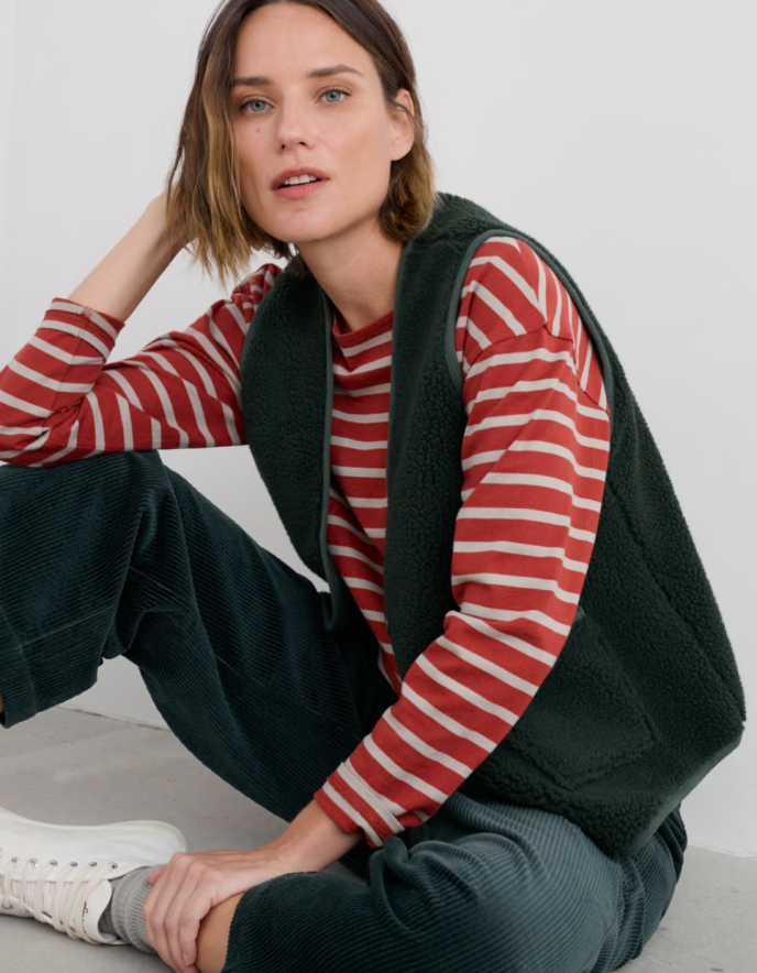 Woman wearing a red and white striped shirt with a black vest sitting on a light-colored floor.