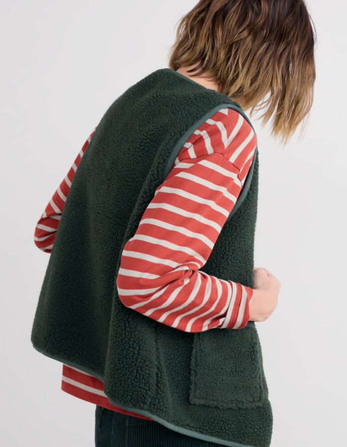Person wearing a green fleece vest over a red and white striped shirt on a plain background
