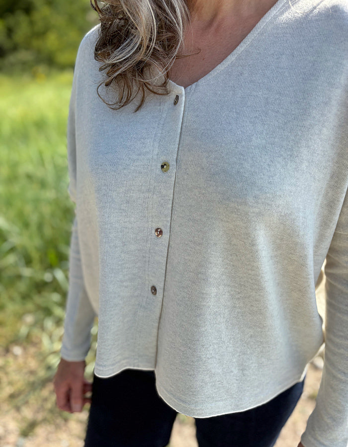 Person wearing a light winter white button-up cardigan outdoors with greenery in the background