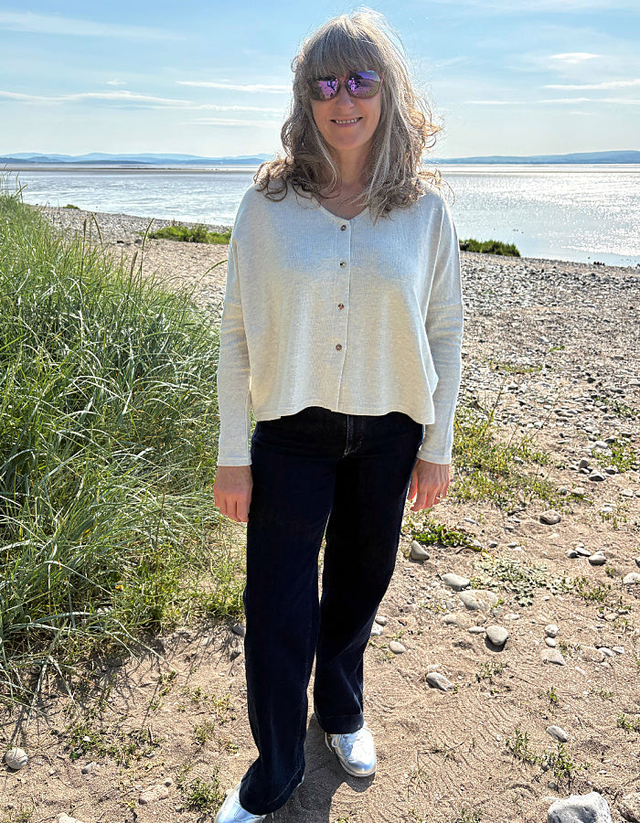 Person wearing a light winter white button-up cardigan outdoors with greenery in the background