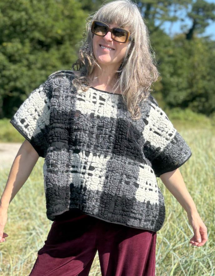 Woman wearing a black and white checkered crochet top in a grassy outdoor setting