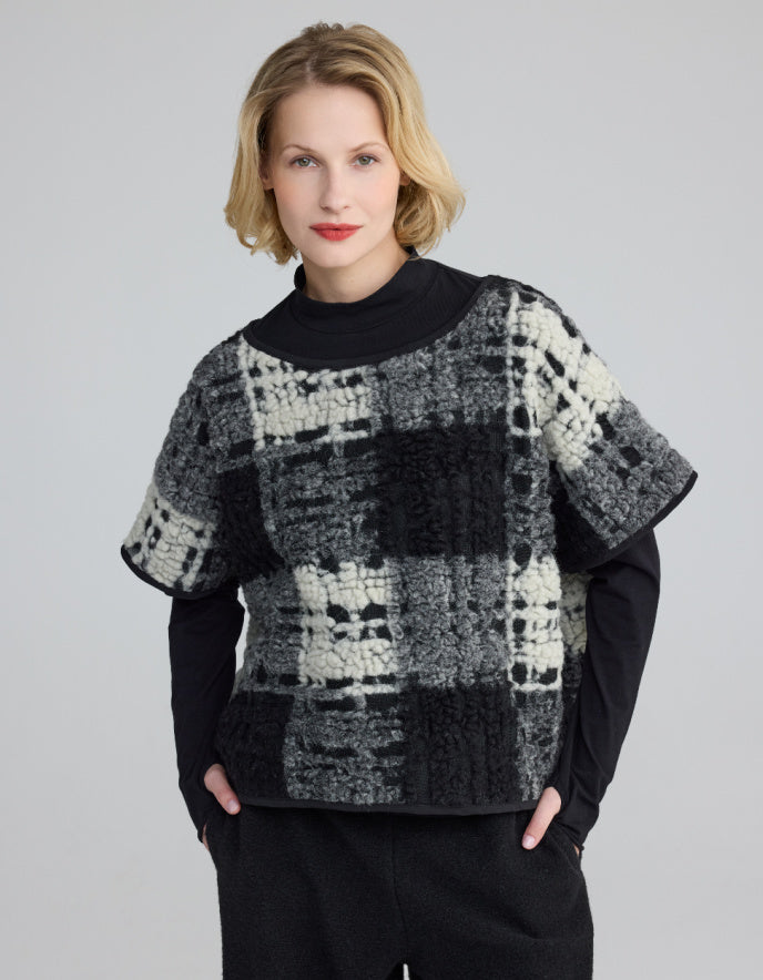 Woman wearing a black and white patterned sweater over a black turtleneck on a gray background