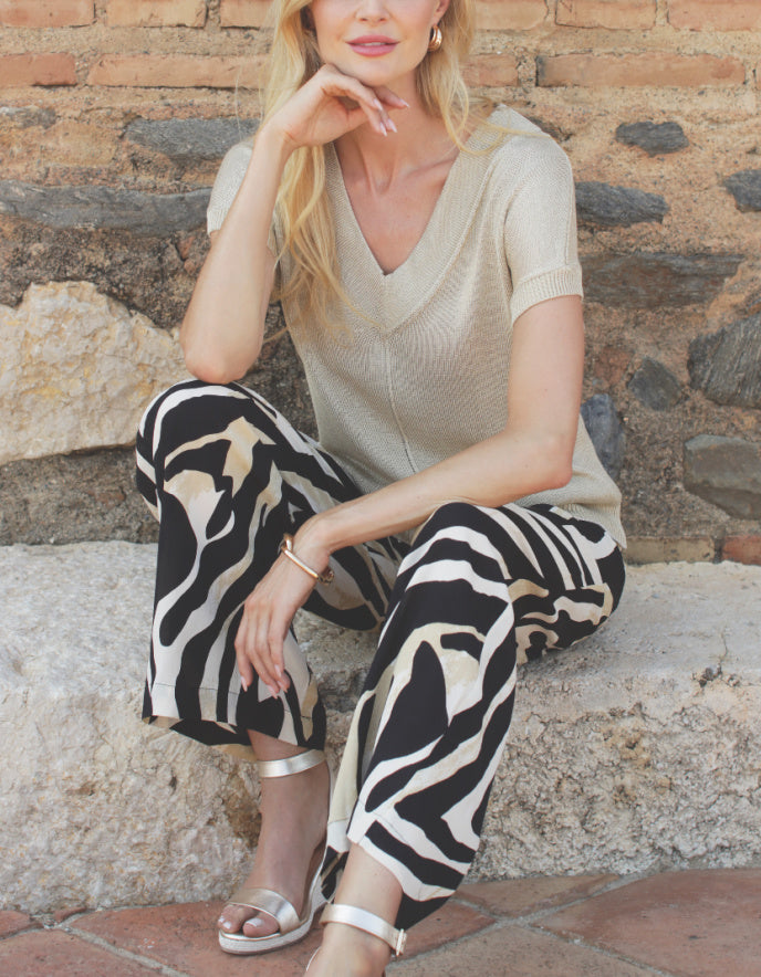 Woman sitting on stone steps wearing a beige top and zebra print pants.