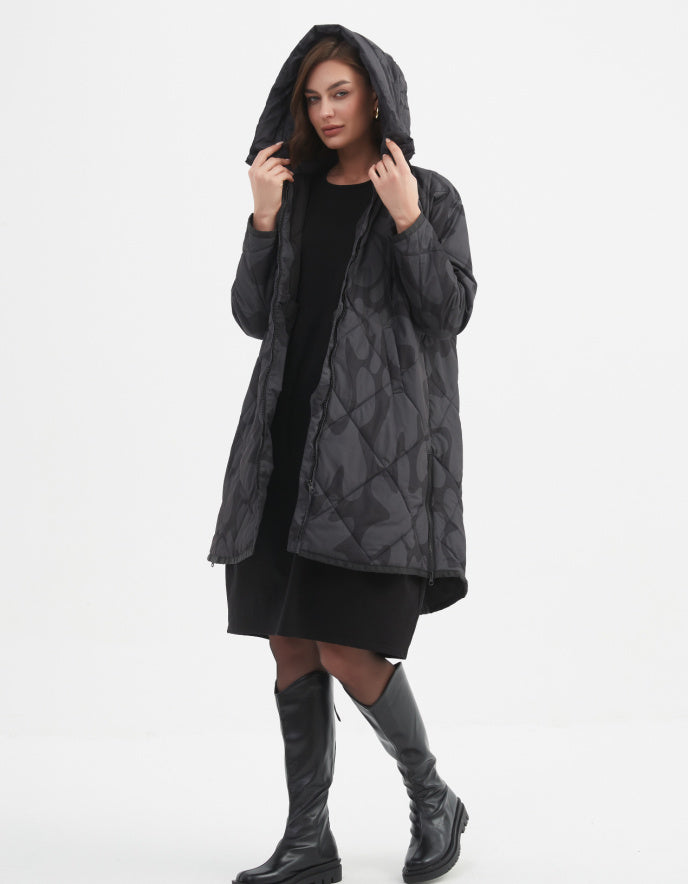 Woman wearing a dark grey and black blot print hooded coat on a white background
