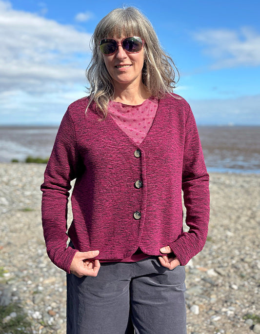 Woman wearing a pink cardigan on a beach with a blue sky.