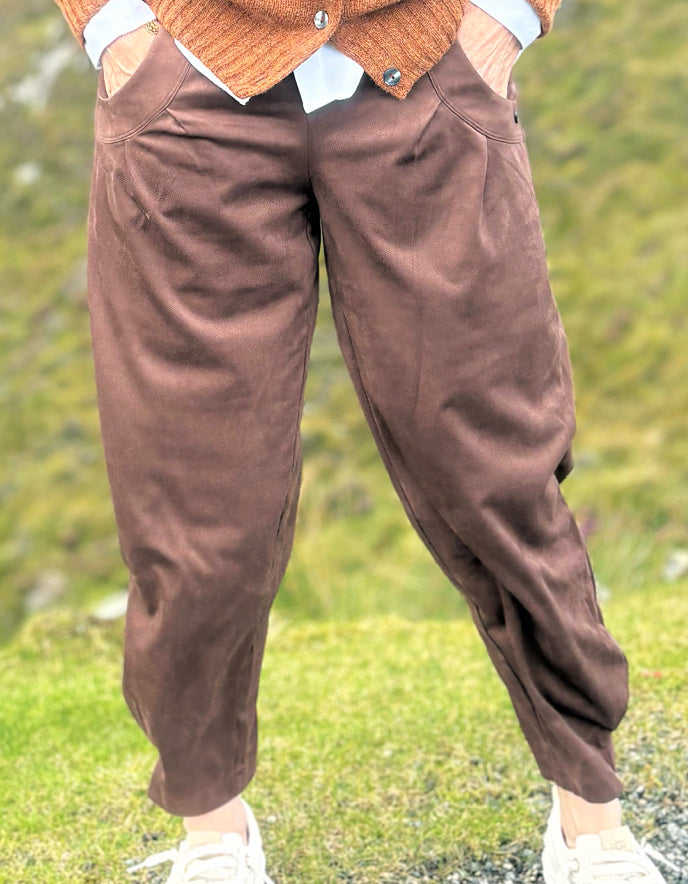 A person wearing brown corduroy pants with a brown cardigan and white sneakers, standing outdoors on a grassy hillside.
